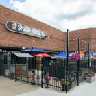 Outdoor patio of Smash House restaurant with black metal fencing, tables, umbrellas, and hanging flower baskets