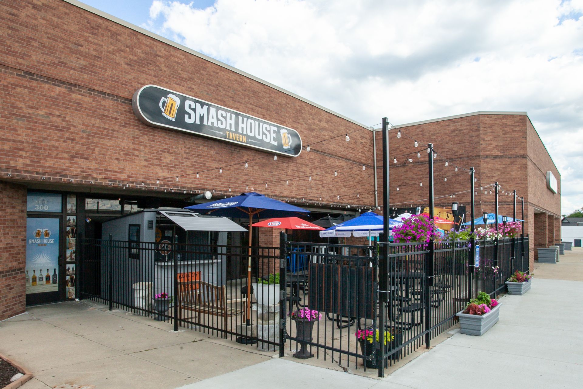 Smash House restaurant exterior with fenced patio, colorful umbrellas, and flower planters