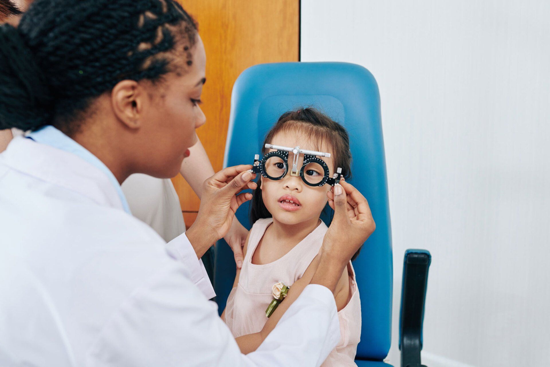 An eye care professional conducting a vision examination for a young patient using a trial frame.