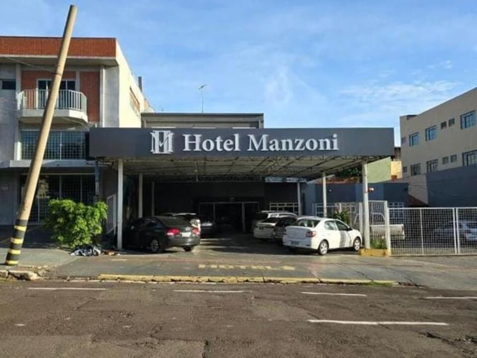 Fachada do Hotel Manzoni com carros estacionados e um céu azul límpido.