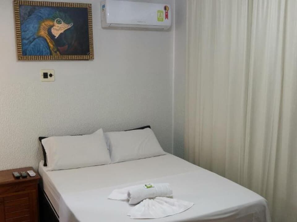 Quarto de hotel impecavelmente arrumado, com cama, toalhas em forma de cisne, cortinas e uma pintura colorida na parede.