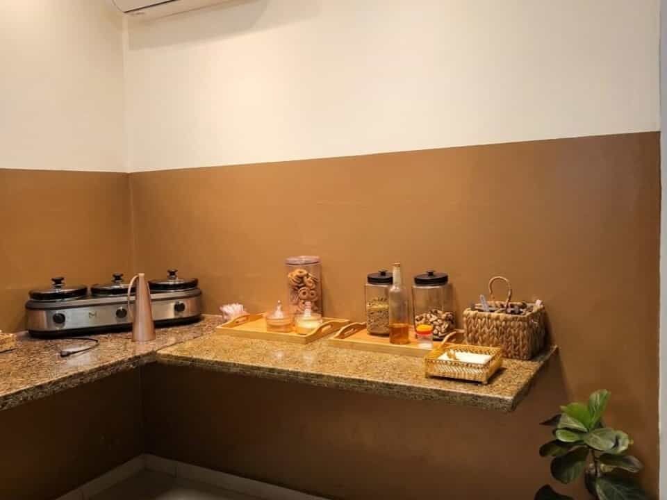 Mesa de buffet com pratos cobertos, potes e petiscos sobre uma bancada em um ambiente bege.