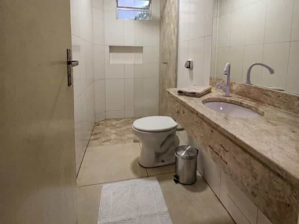 Pequeno banheiro bege com vaso sanitário, pia, toalha e janela.