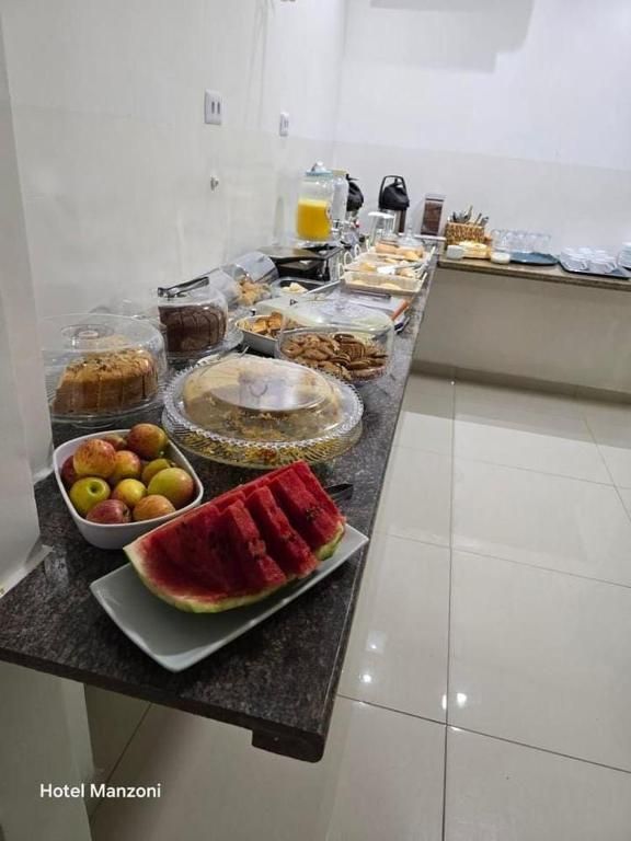 Buffet de café da manhã do hotel com frutas, doces e fatias de melancia em uma bancada preta.