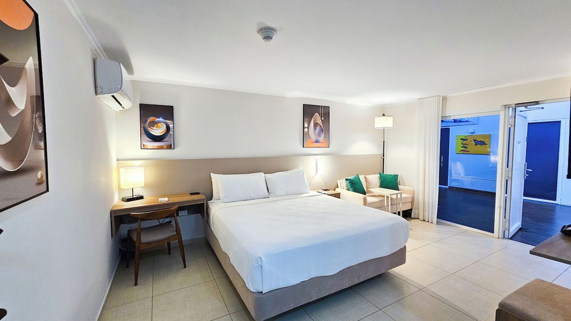Habitación de hotel con una cama, un escritorio, dos sillas y una puerta.