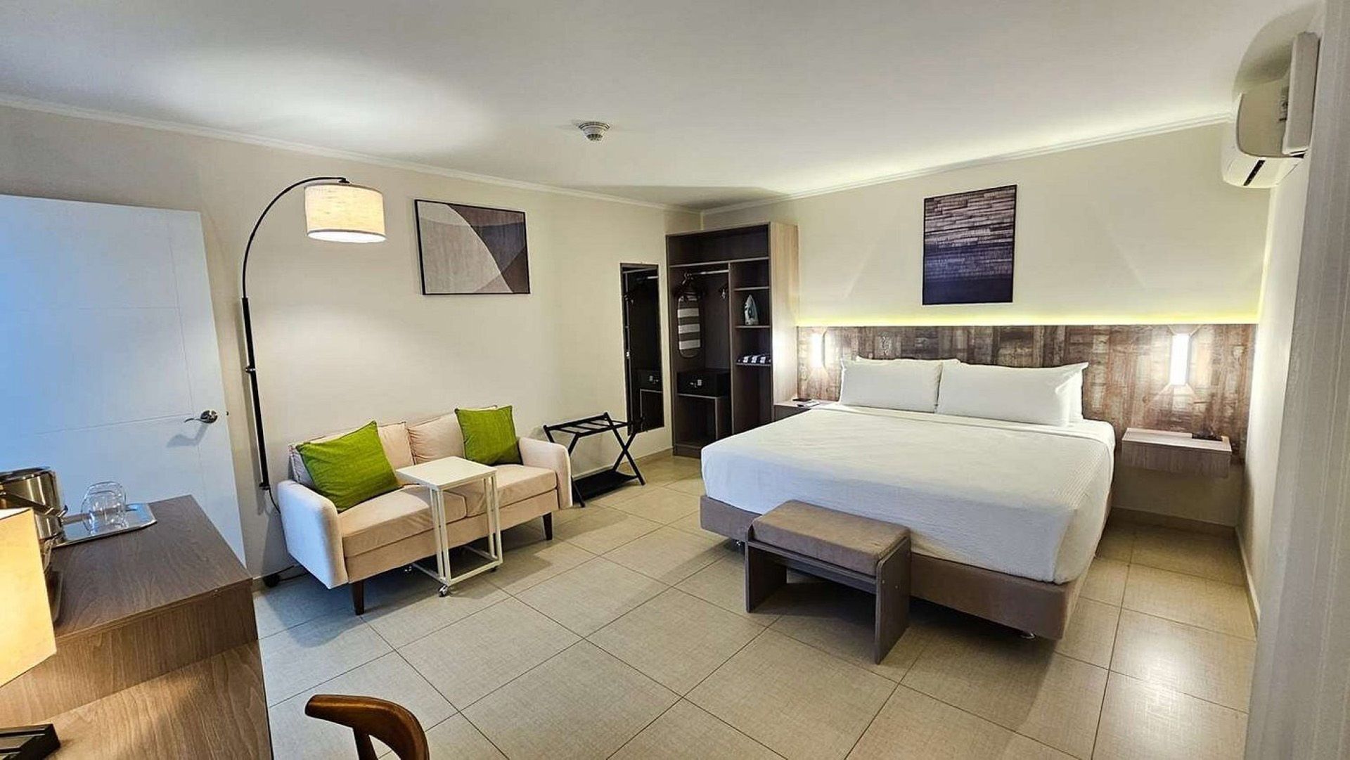 Habitación de hotel con cama, sofá, escritorio, armario, arte en las paredes y suelo de baldosas.