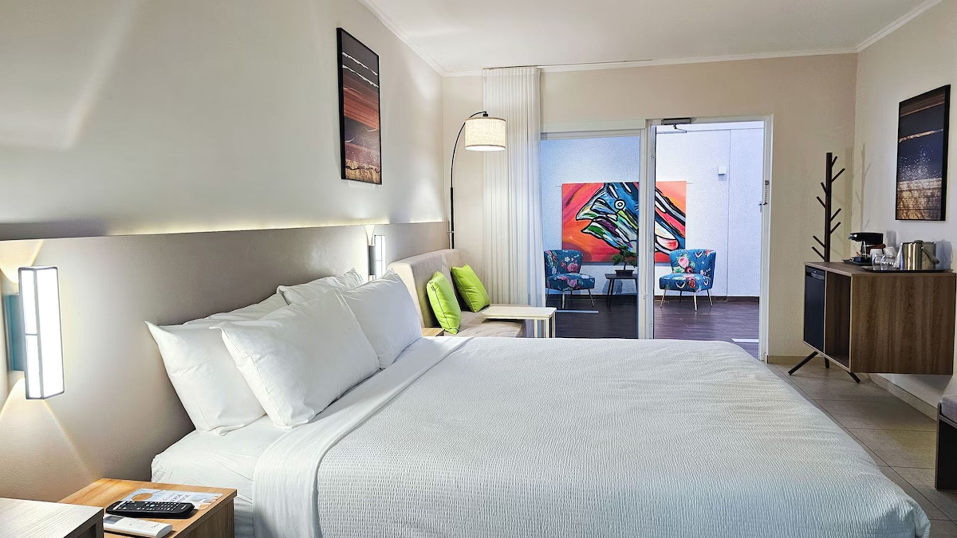 Habitación de hotel con una cama, un pequeño sofá y puerta de entrada a una colorida zona de estar al aire libre.