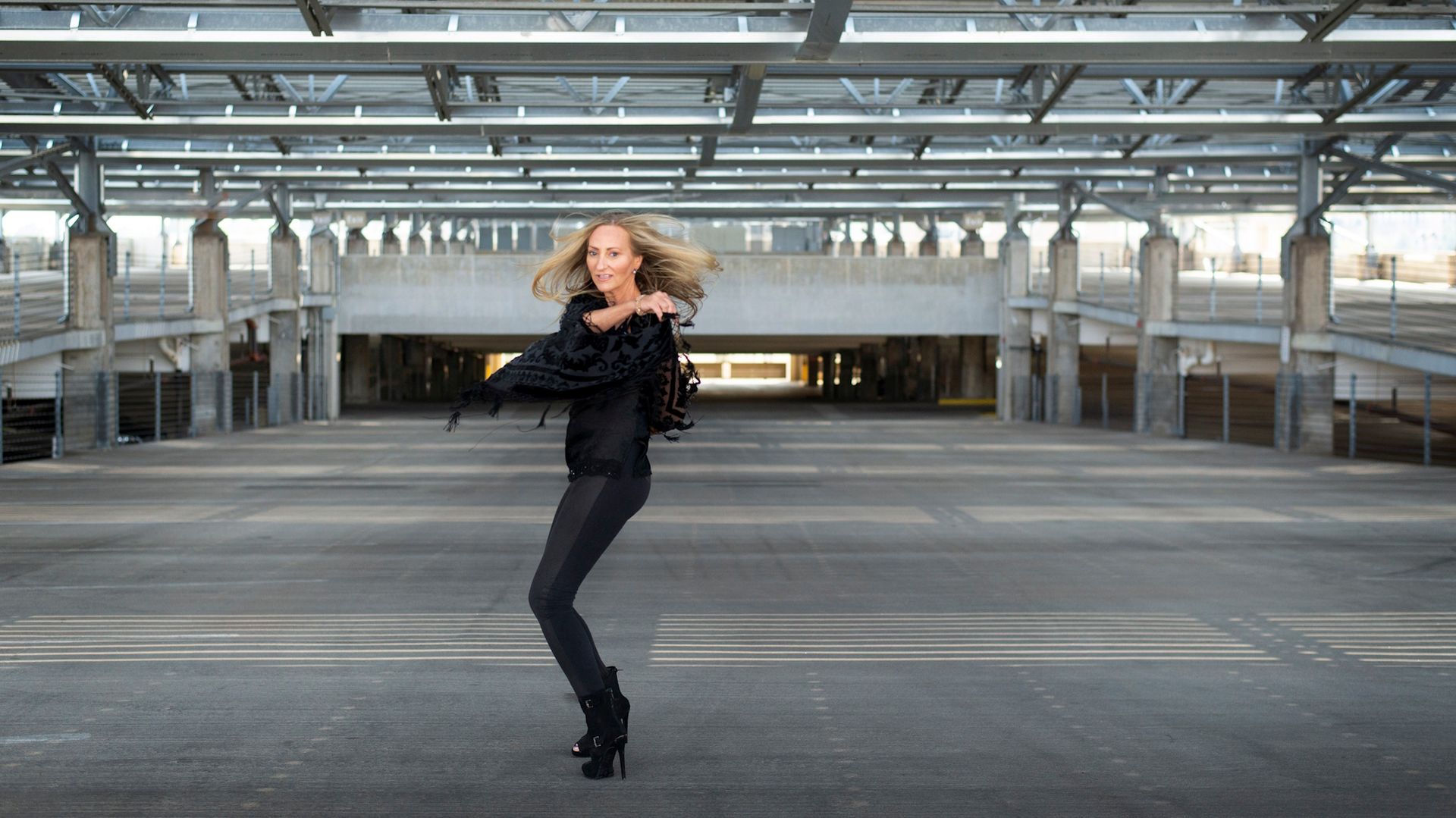 Woman dancing in black outfit in an empty industrial parking structure
