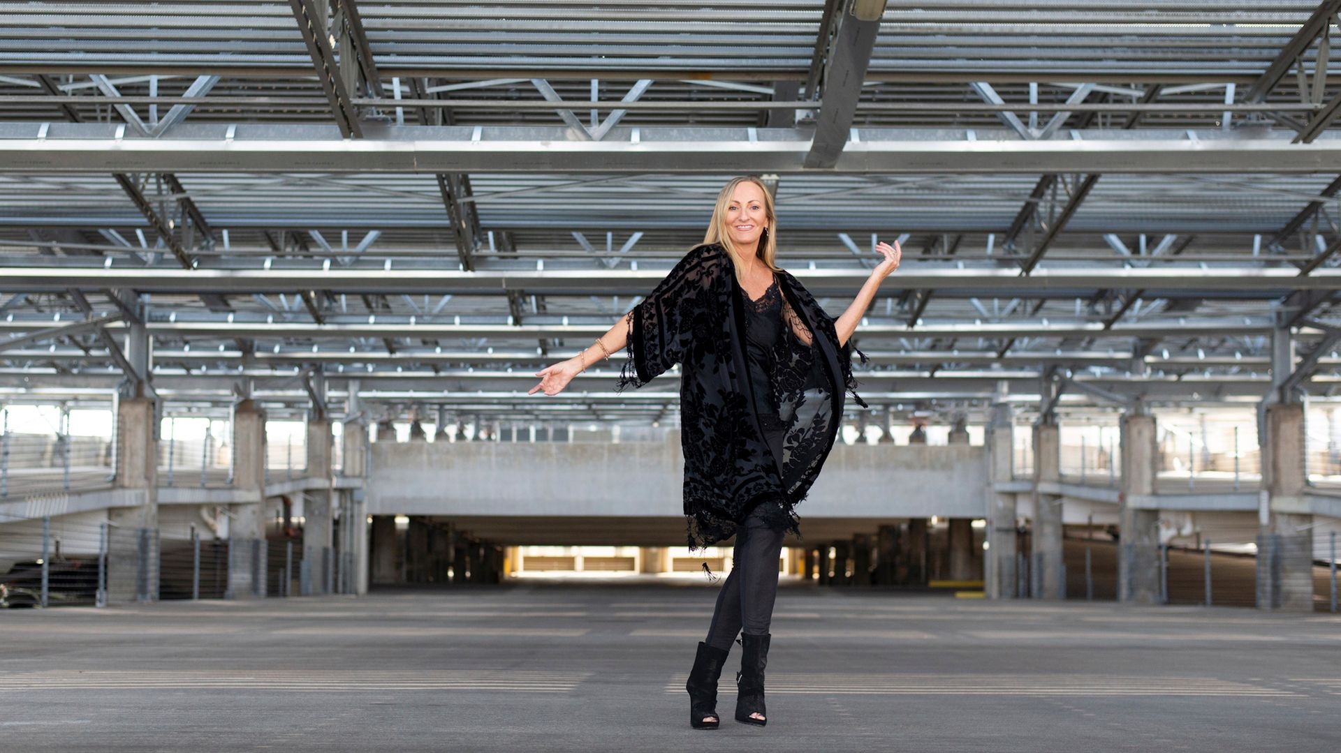 Woman posing in a black outfit inside a large empty industrial hall