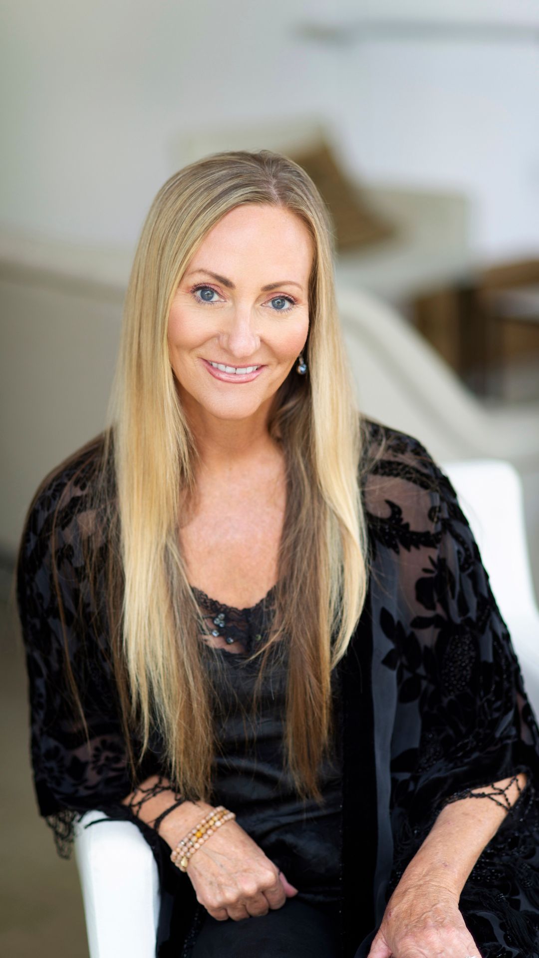 Smiling woman in a black lace top seated indoors on a white chair