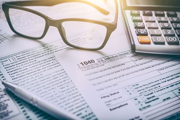 Eyeglasses, calculator, and pen on top of tax forms.