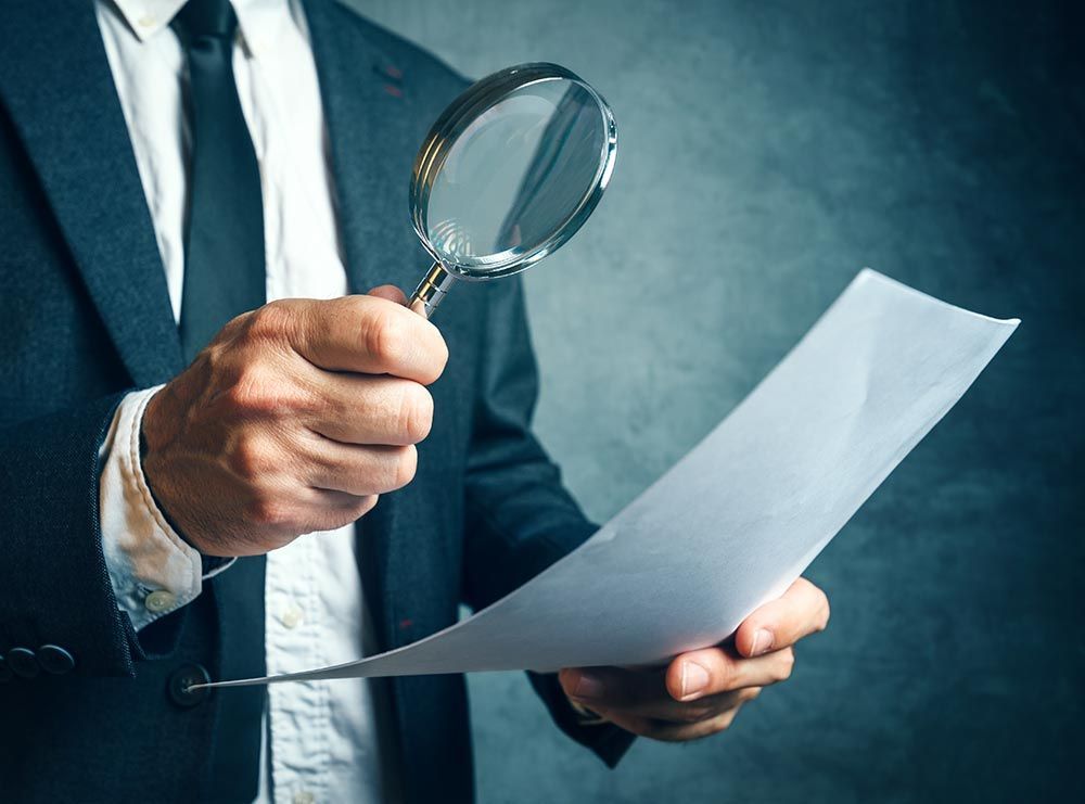 Man in suit uses magnifying glass to examine paper.