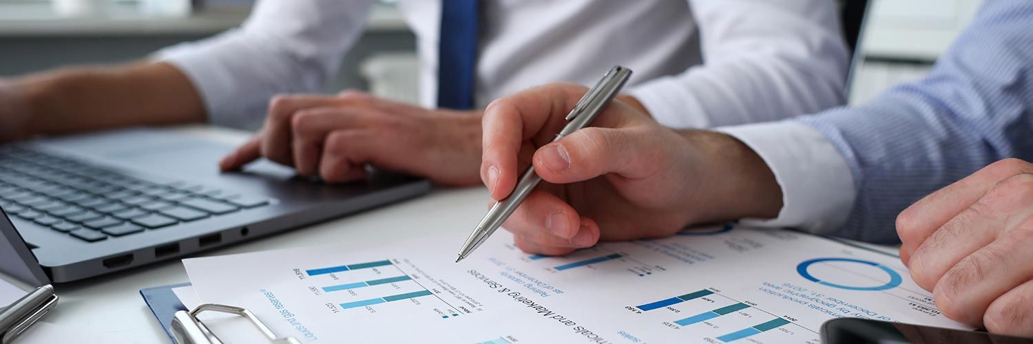 Two people reviewing financial charts with a laptop and pen.