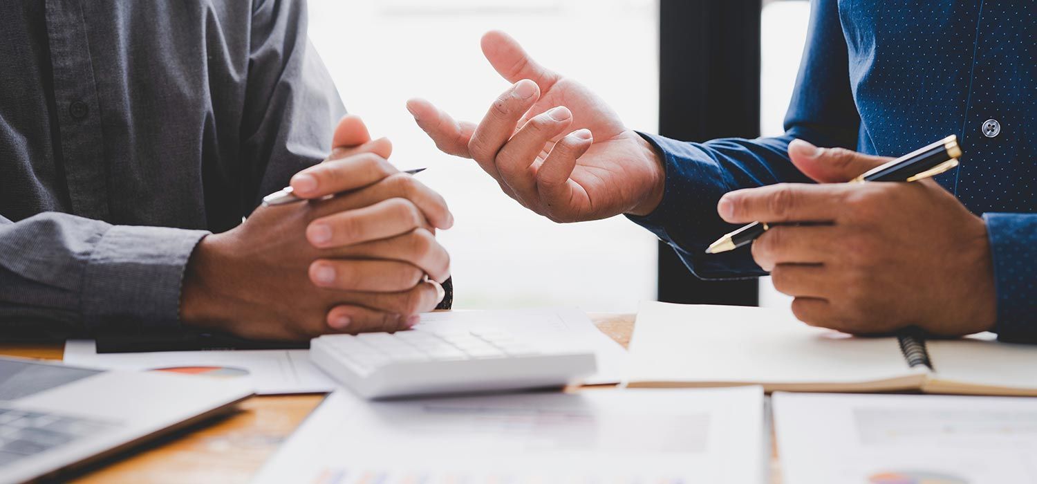 Two people in business attire discussing finances, one gesturing, papers and calculator on the desk.