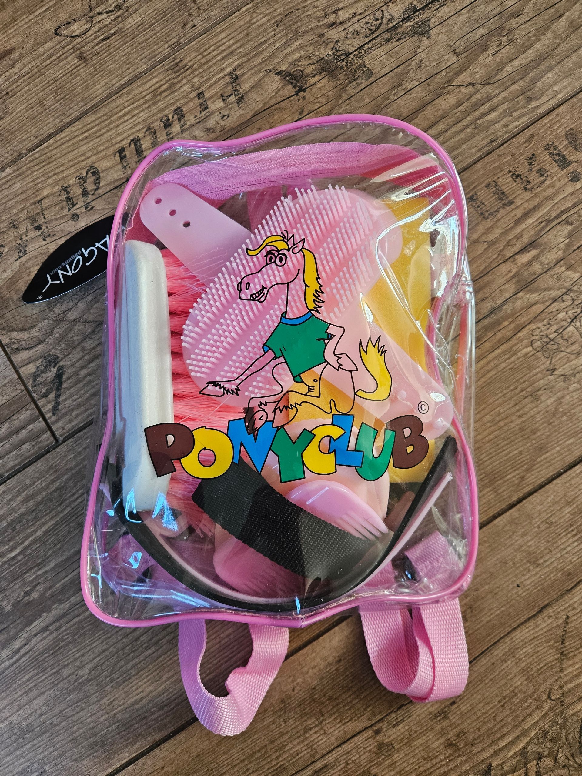 Een roze, doorzichtige plastic rugzak met het Ponyclub-logo, met daarin een set borstels en benodigdheden voor de verzorging van paarden.