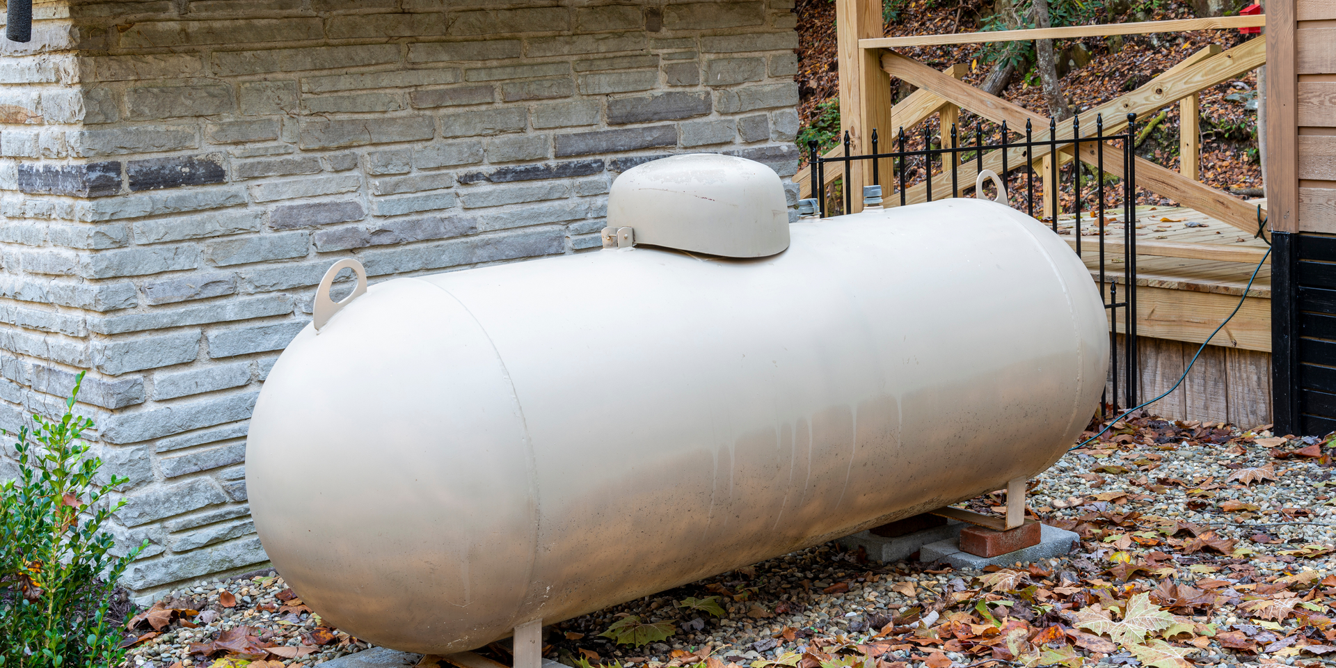 A large white propane tank is sitting in front of a brick building.