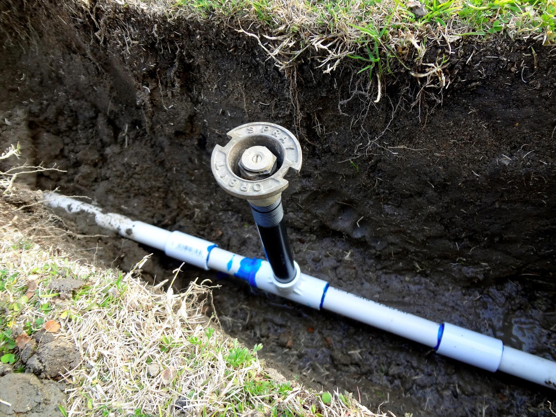 A sprinkler is sitting in the dirt next to a pipe.