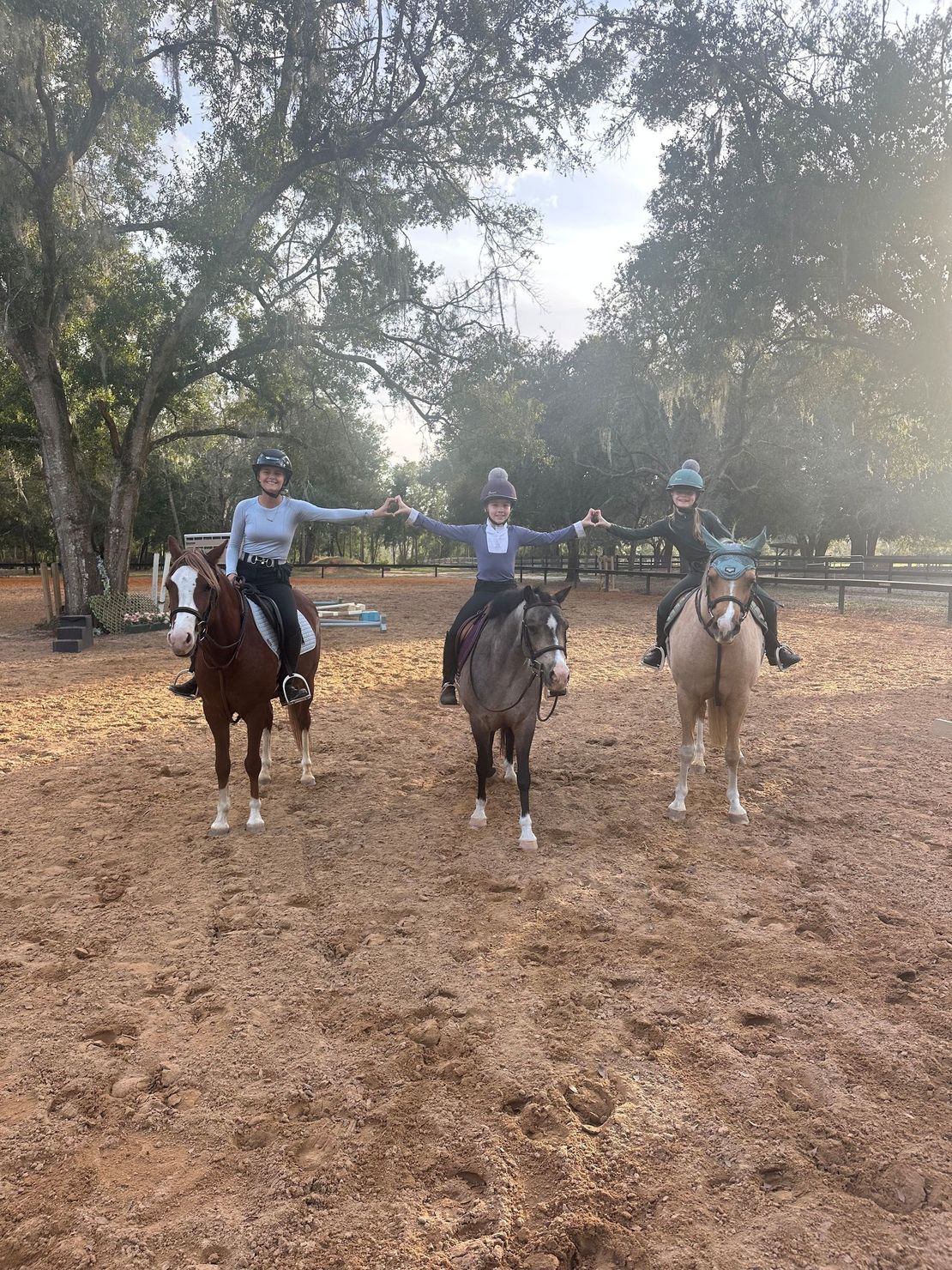 Three riders on horses in a leafy outdoor clearing, facing the camera.