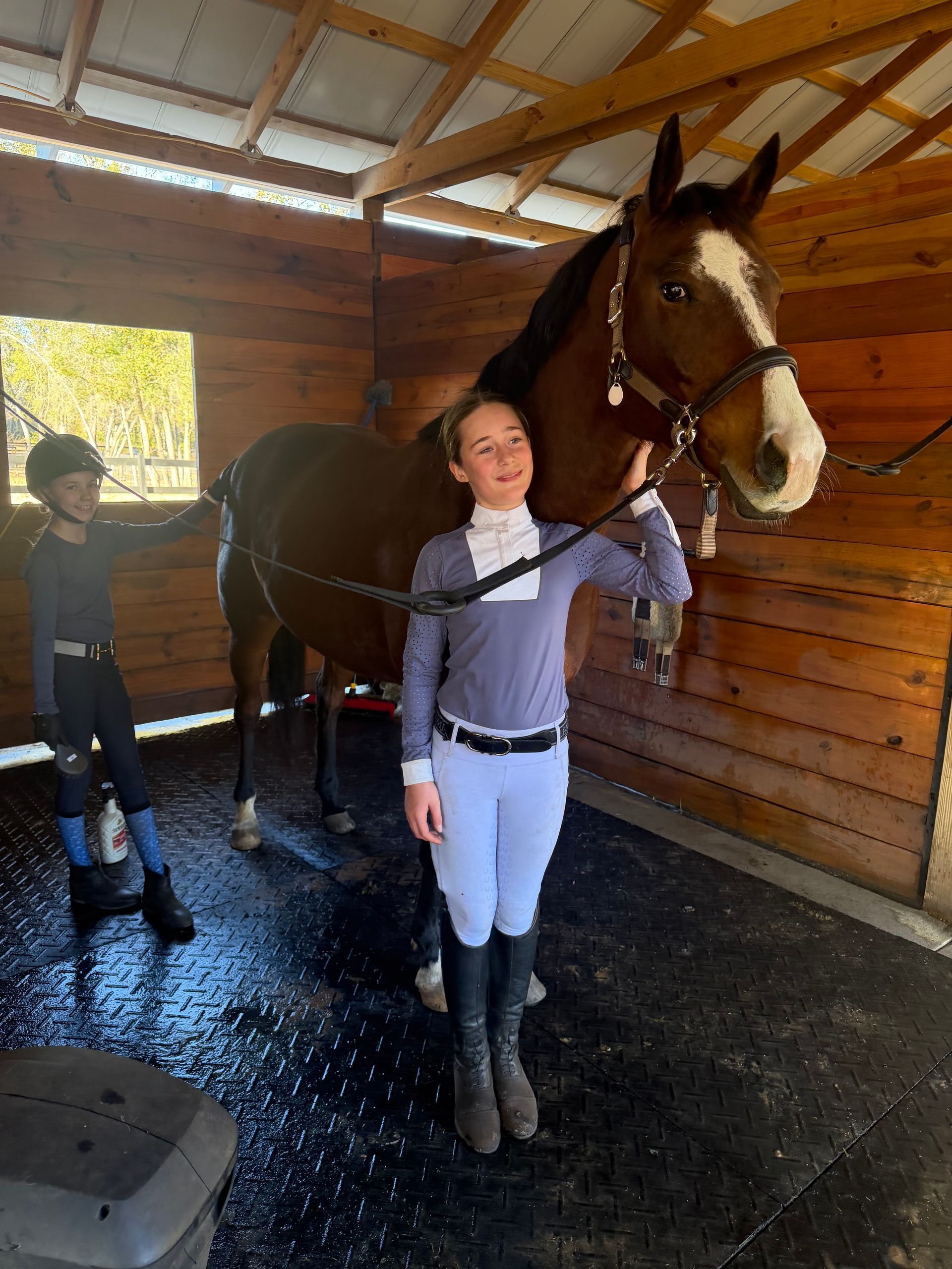 Person standing beside a saddled horse in a wooden stable