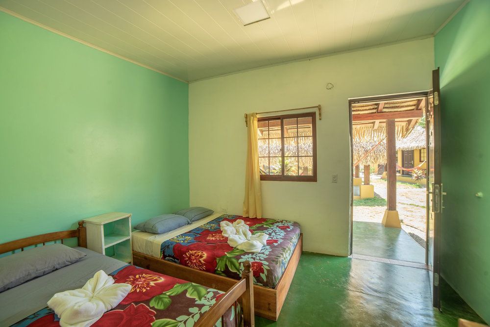 Small bedroom with two beds, green walls, and an open door to a sunny outdoor area