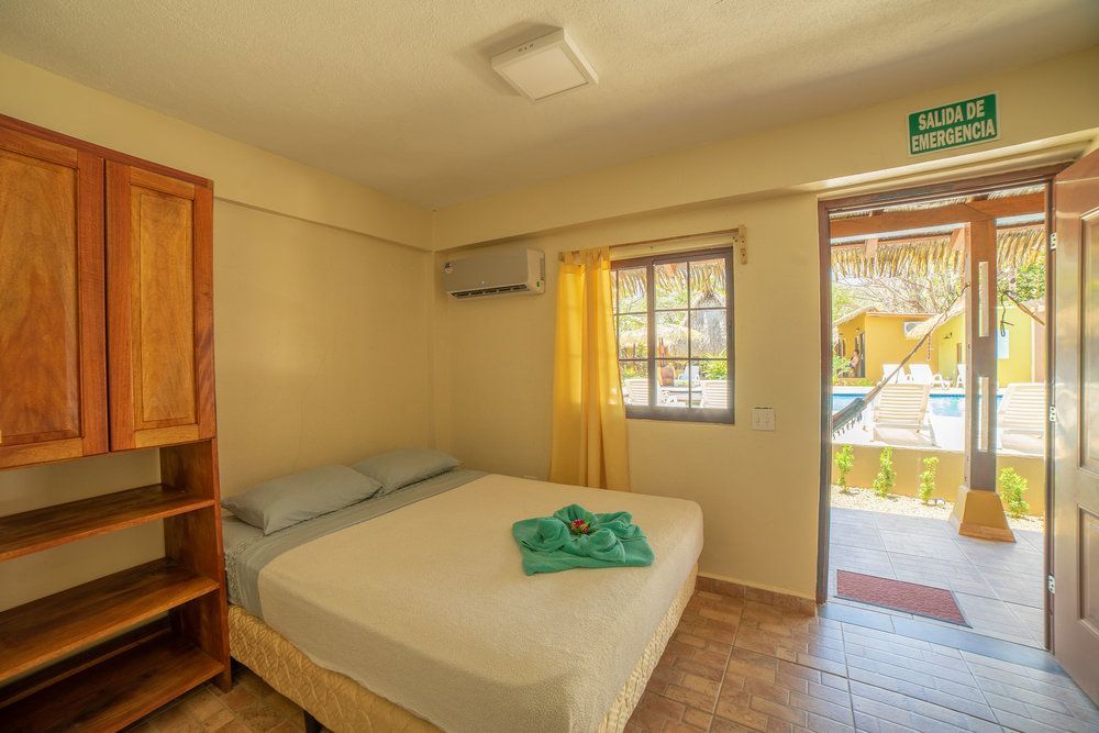 Small bedroom with bed, wooden shelves, window, and open door to a sunny patio.