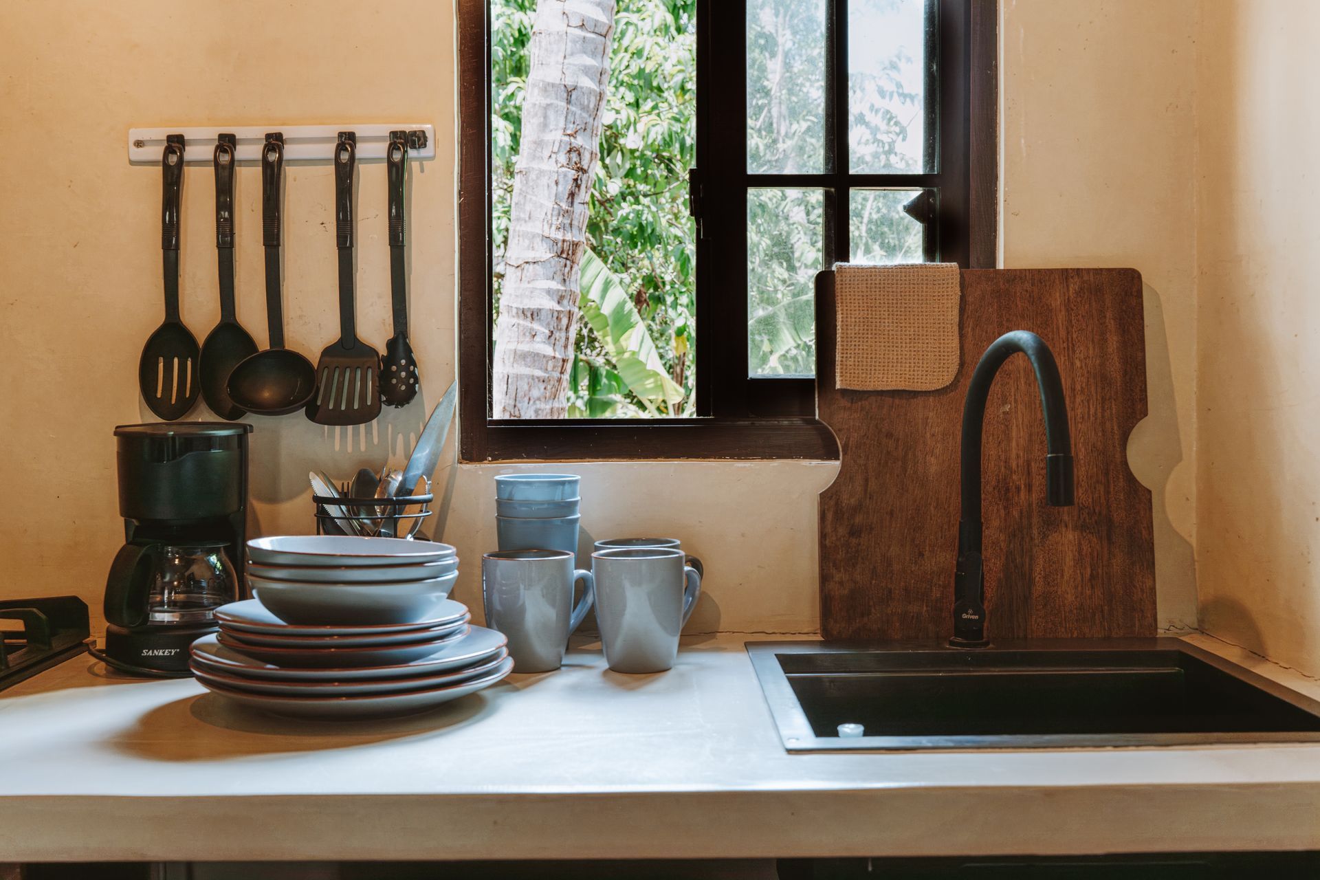 Cozy kitchen corner with stacked dishes, hanging utensils, sink, and sunlit window