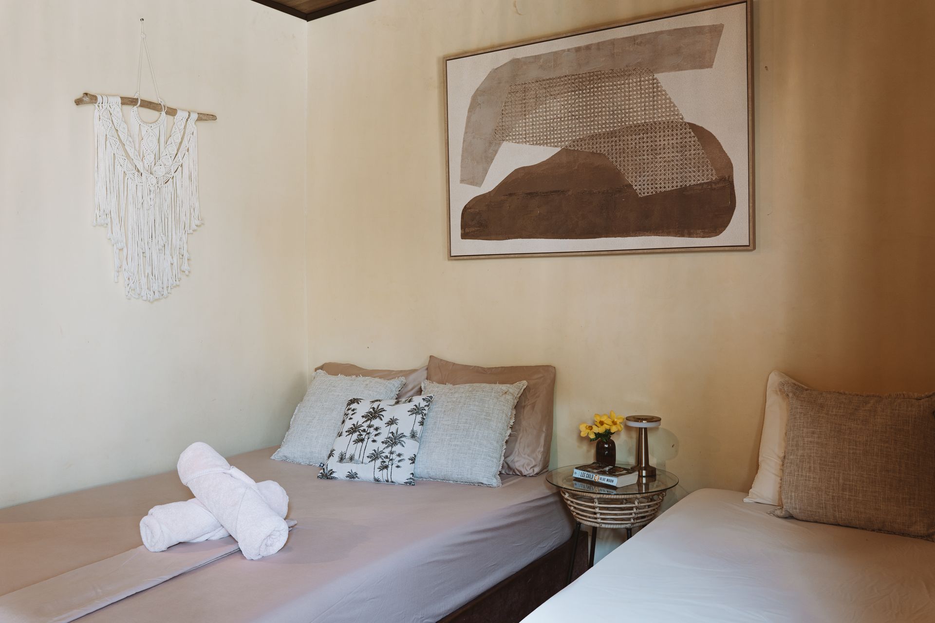 Cozy bedroom with two beds, beige walls, wall art, and a small bedside table with flowers