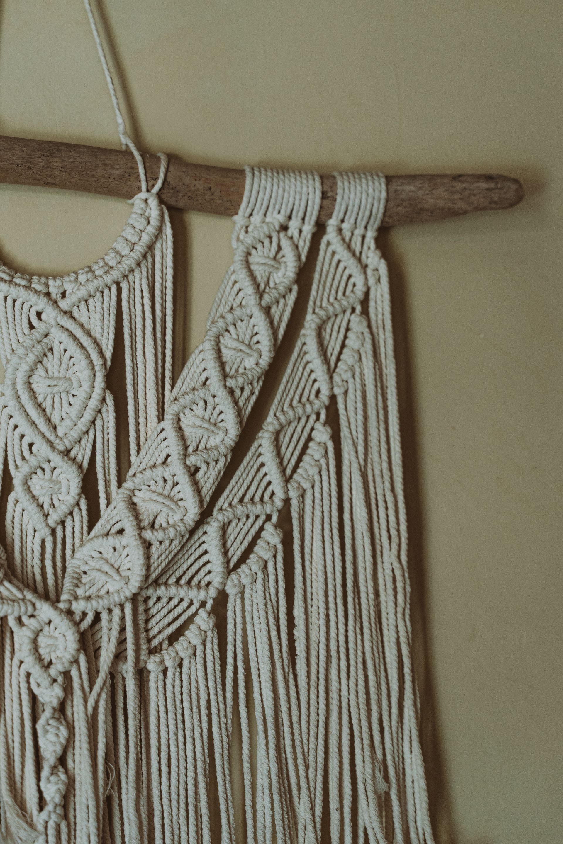 Macramé wall hanging with cream braided leaves and fringe on a wooden dowel
