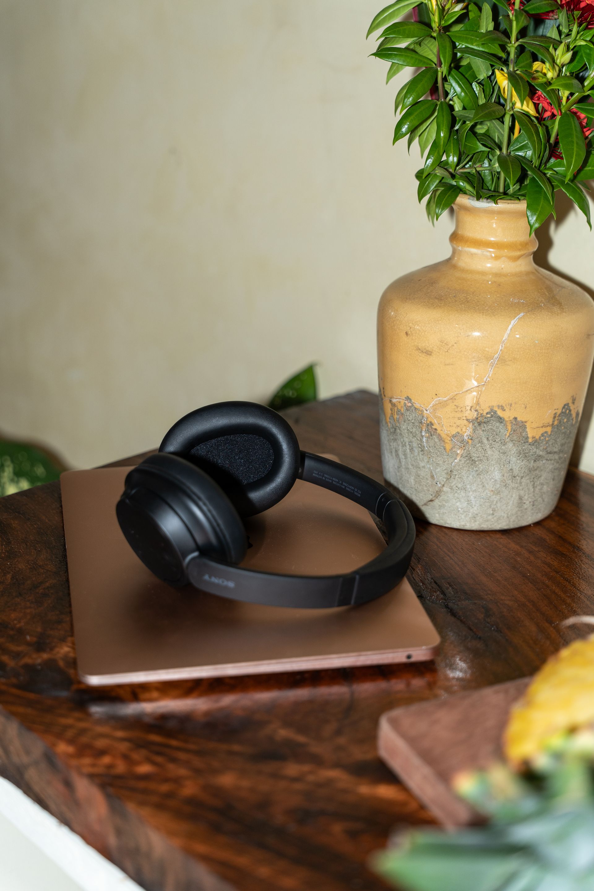 Black headphones on a laptop beside a beige vase with greenery on a wooden table