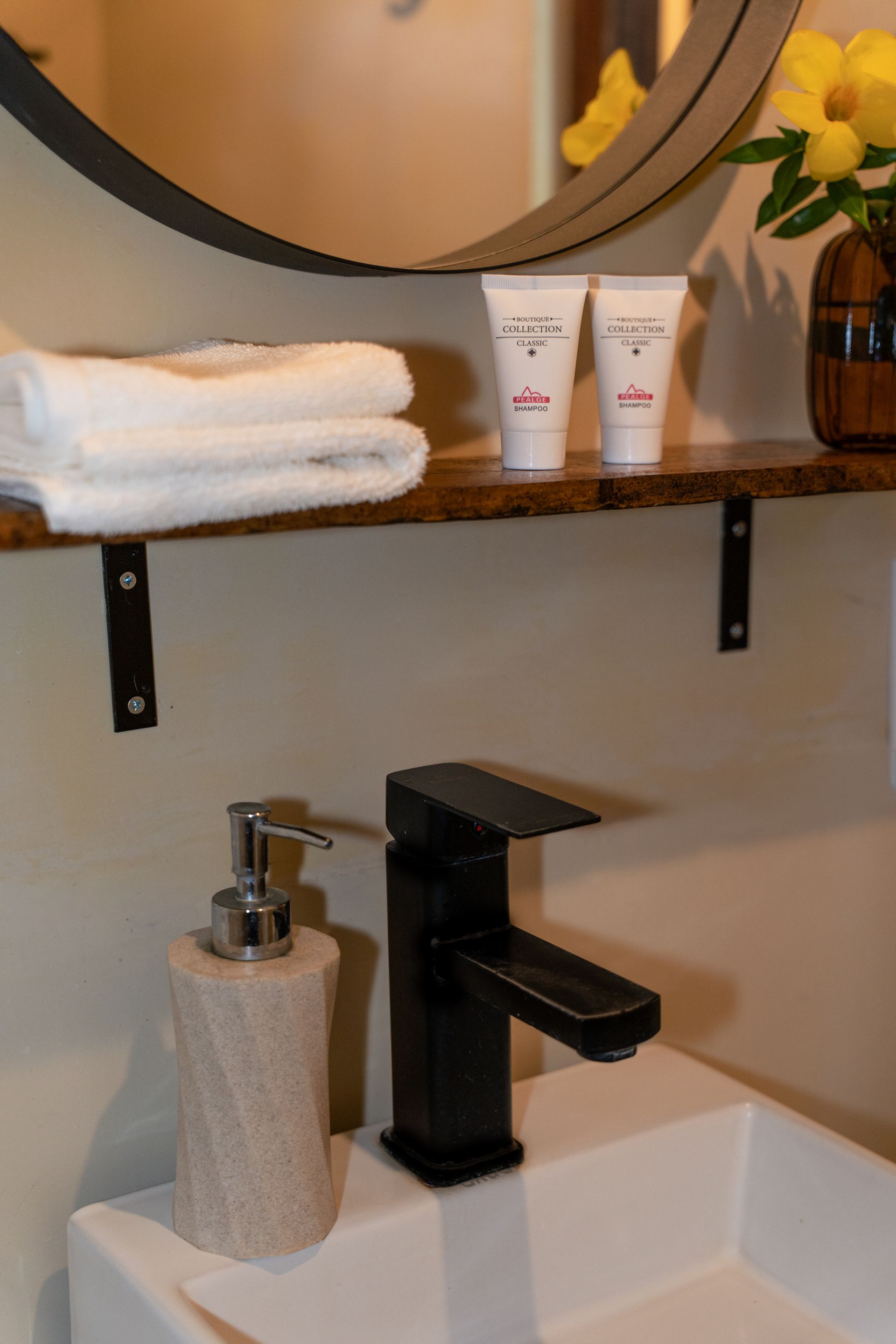 Bathroom sink with black faucet, soap dispenser, folded towels, mirror, and yellow flowers on a shelf