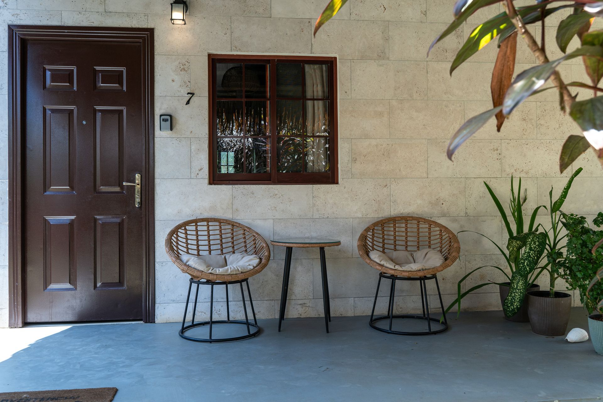 Front porch with dark wooden door, window, two wicker chairs, small table, and potted plants