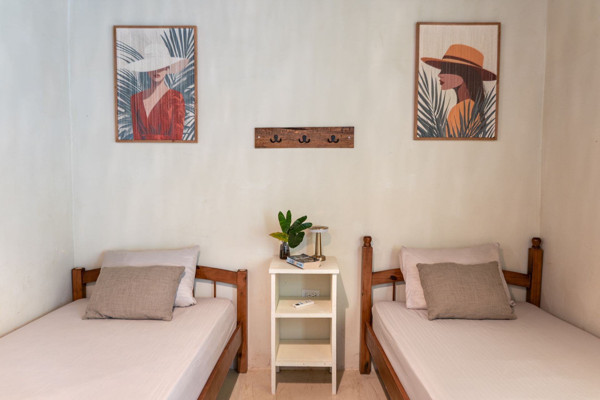 Two twin beds in a minimalist room with wall art and a small bedside table with a plant.