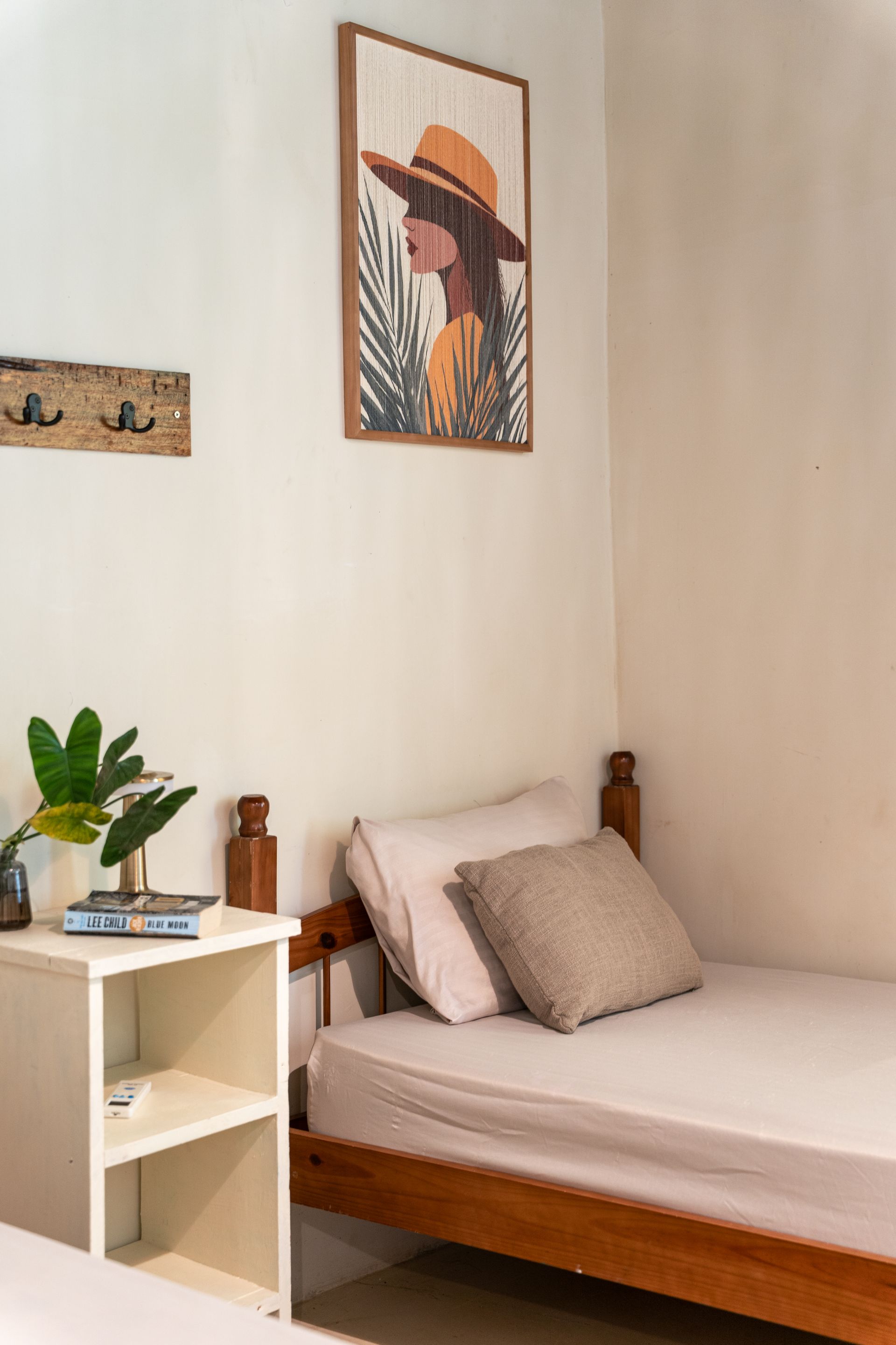 Cozy bedroom corner with a wooden bed, white side table, potted plant, and wall art.