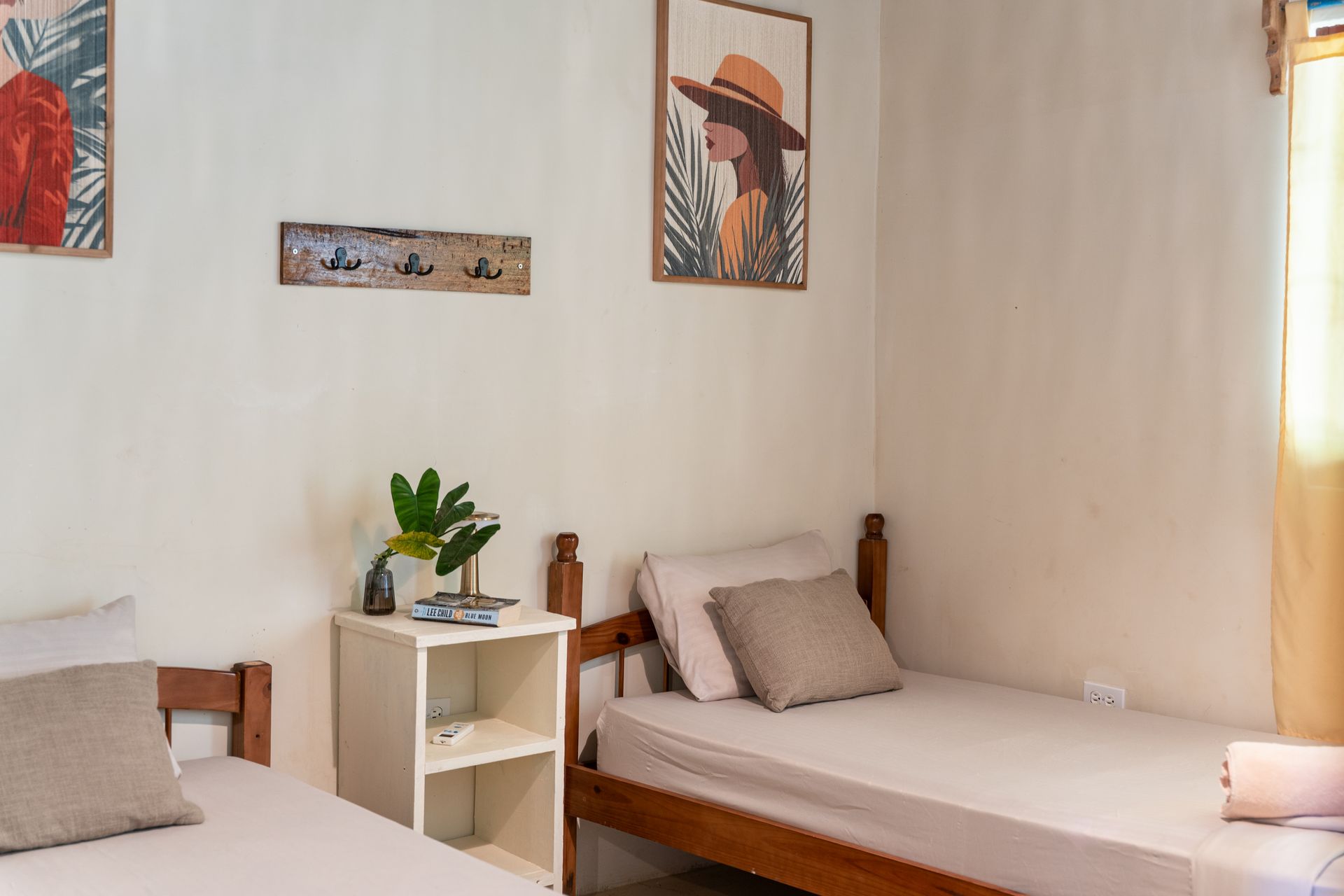 Small minimalist bedroom with two single beds, white walls, and a window with curtains.