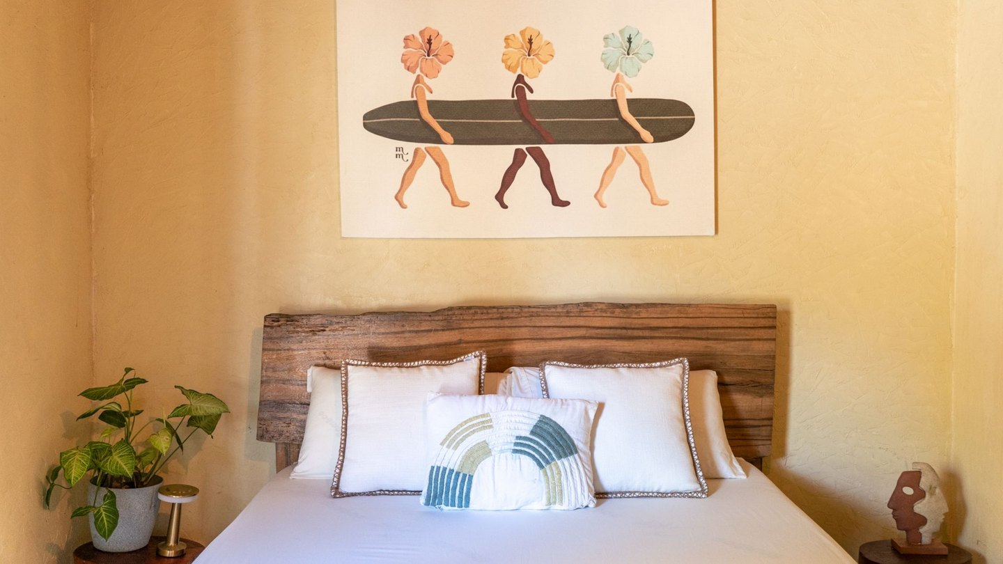 Cozy bedroom with a bed, leaf-pattern pillow, potted plant, and wall art above the headboard