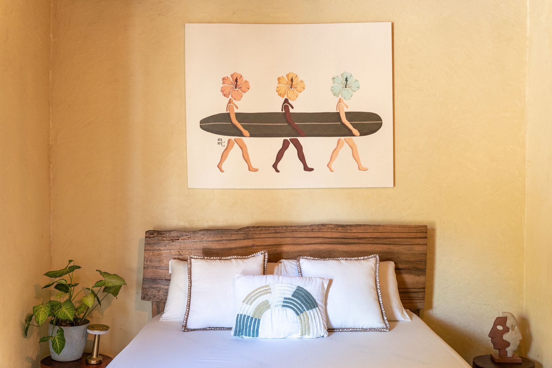 Cozy bedroom with wooden bed, patterned pillows, potted plant, and abstract walking-figure wall art