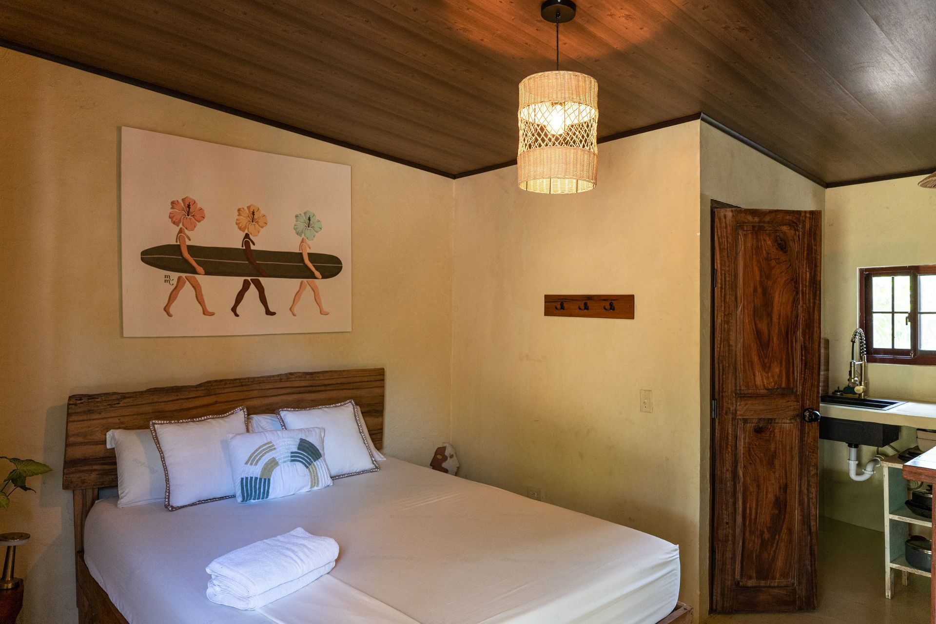 Cozy bedroom with bed, wooden ceiling, hanging lamp, wall art, and open doorway to a bathroom