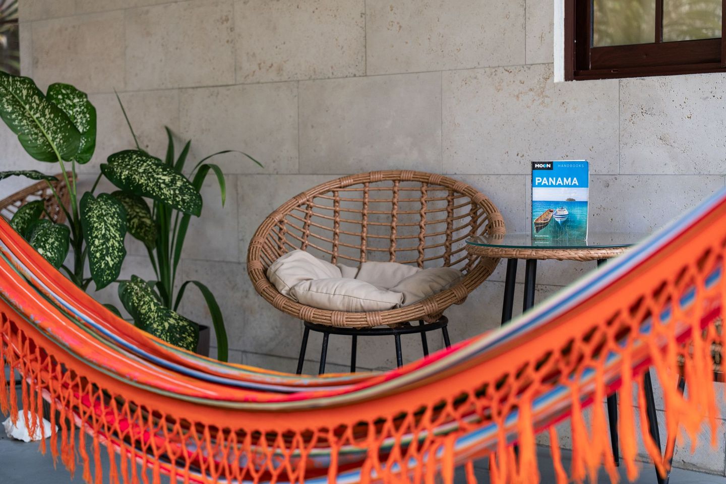 Orange hammock in front of a wicker chair, potted plant, and small table on a stone porch.