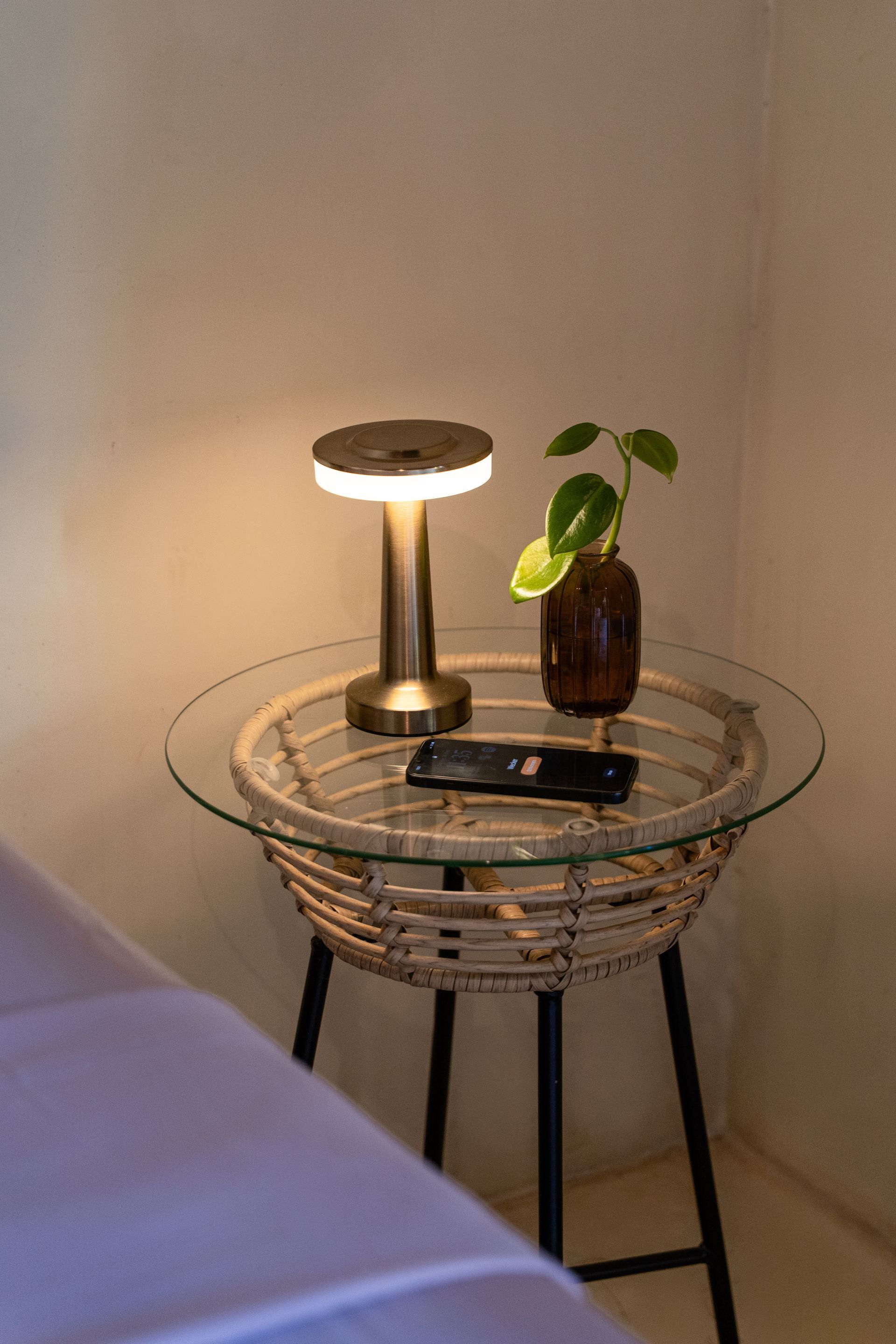 Small round side table with lamp, plant, and remote against a beige wall