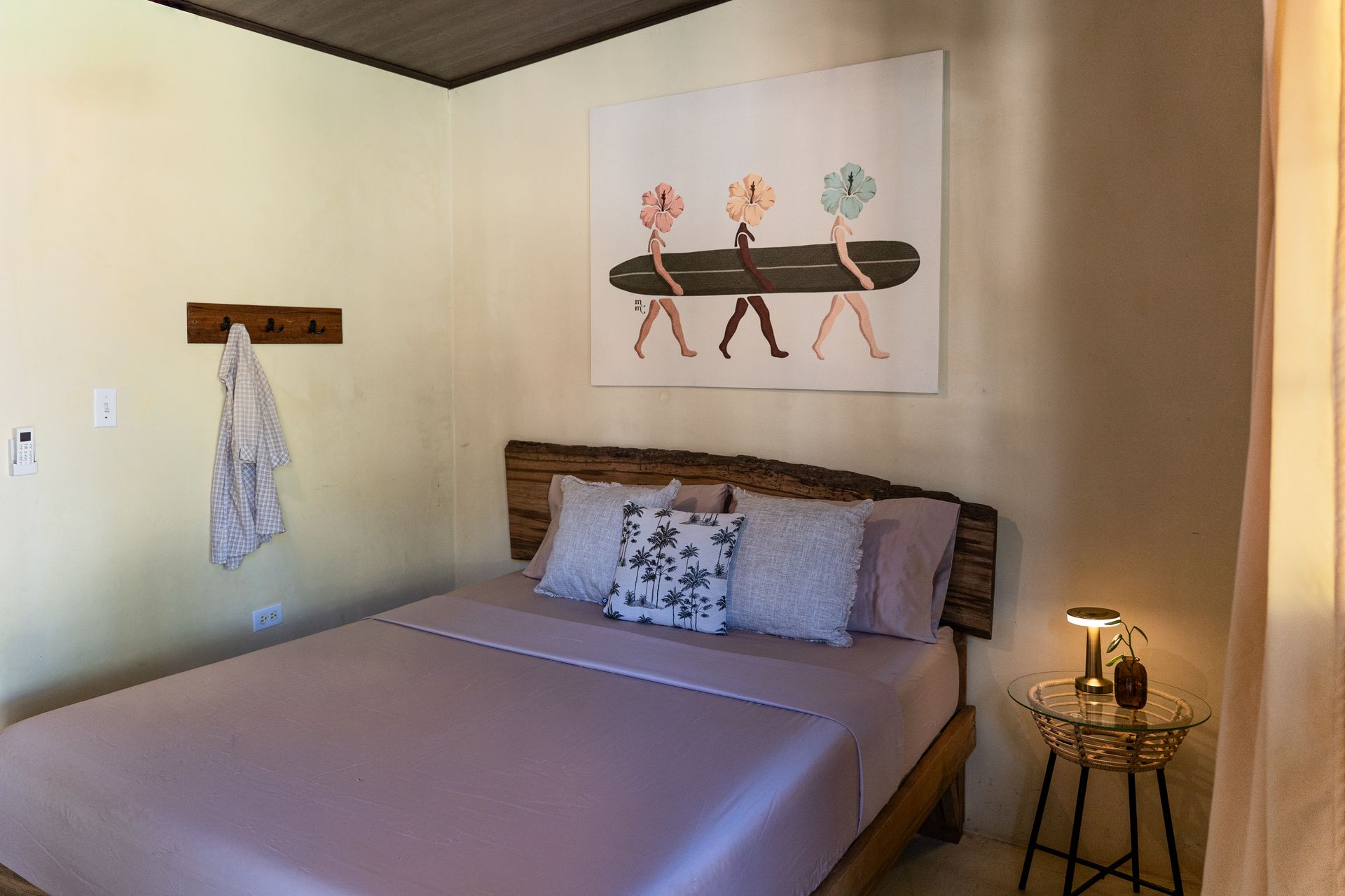 Cozy bedroom with wooden bed, floral wall art, bedside lamp, and a hanging robe.