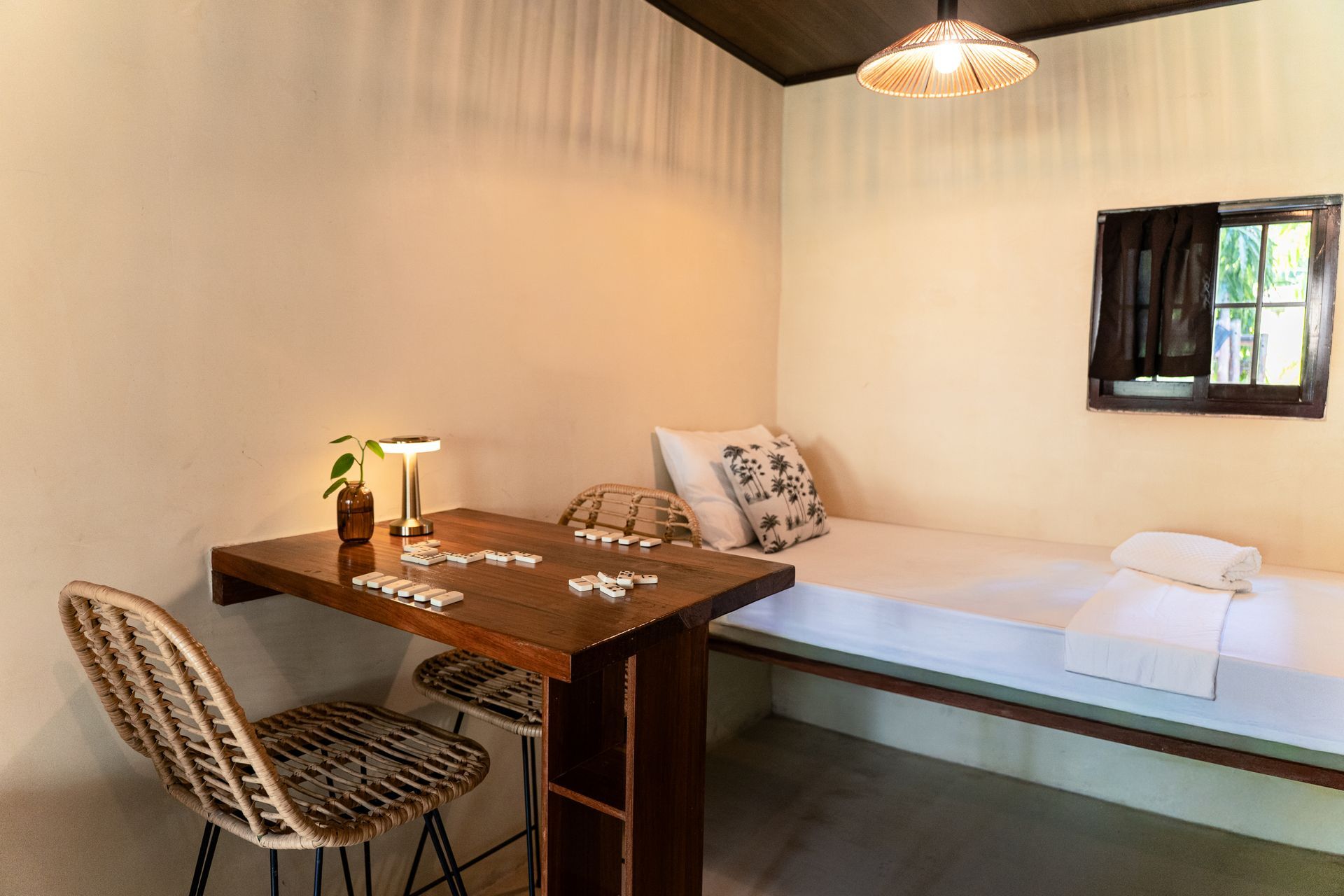 Simple bedroom with a single bed, wooden table, patterned chair, and window.