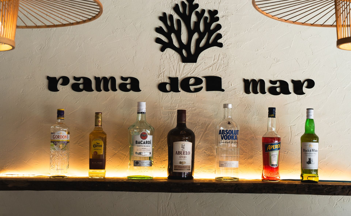Rama del Mar bar shelf with liquor bottles and warm backlit wall decor