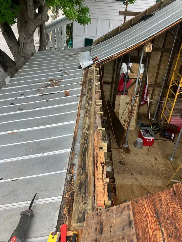 Roofing work in progress on a house, with exposed framing and metal roofing panels removed.