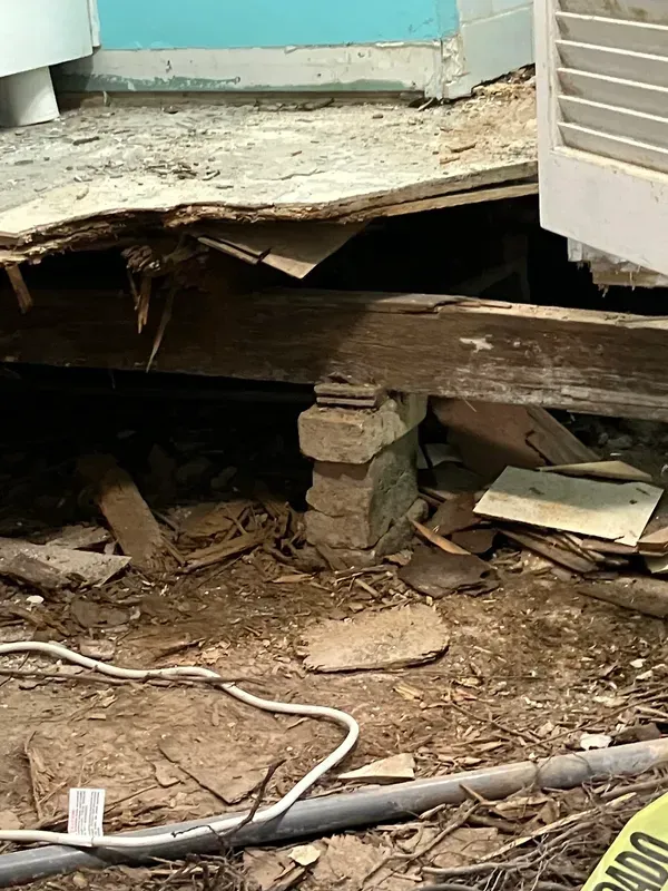 Collapsed porch floor with exposed wooden beams, debris, and a damaged support post.