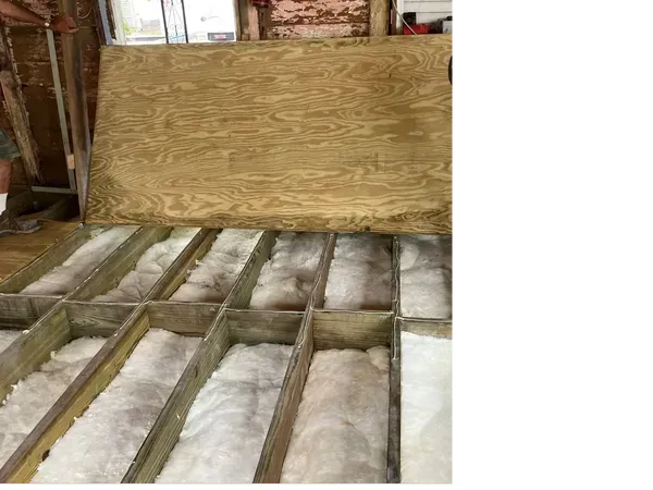 Insulated wooden floor framing in a building under construction with a plywood wall in back