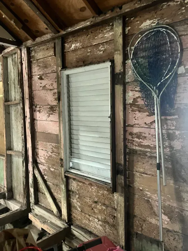Old shed wall with weathered wood, a small white window, and a hanging tennis racket.