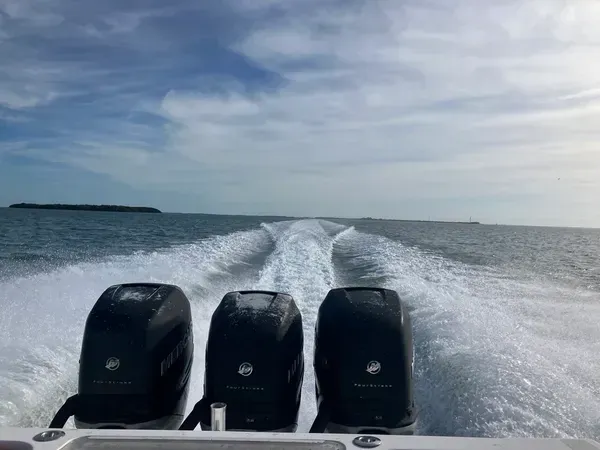 Three outboard motors powering a boat across open water, leaving a white wake under a cloudy sky