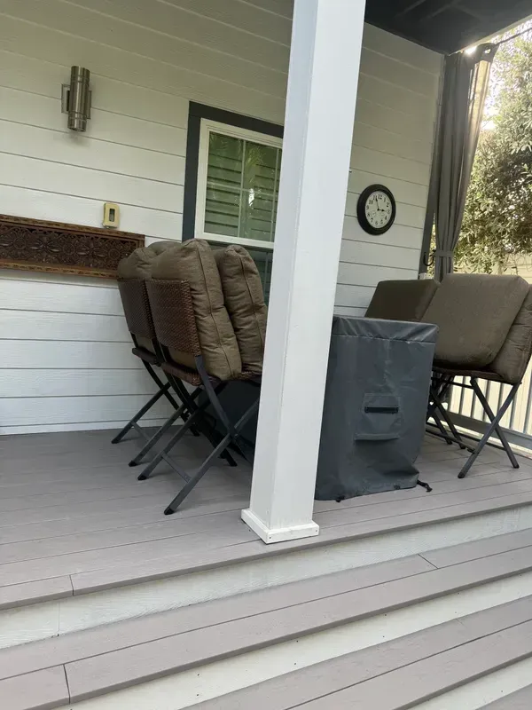 Covered porch with patio chairs, a table, and a front column on a gray deck.