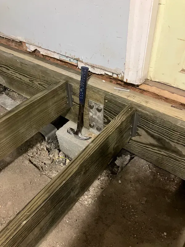 Concrete floor opening with exposed blue pipe and damaged wood framing near a doorway