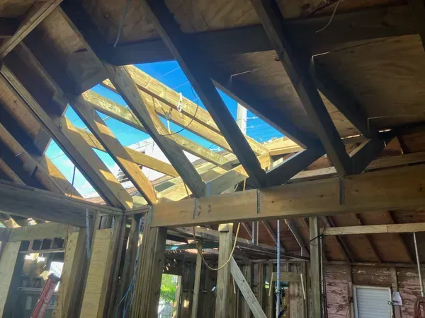 Damaged wooden roof with missing panels exposing blue sky inside a building under construction